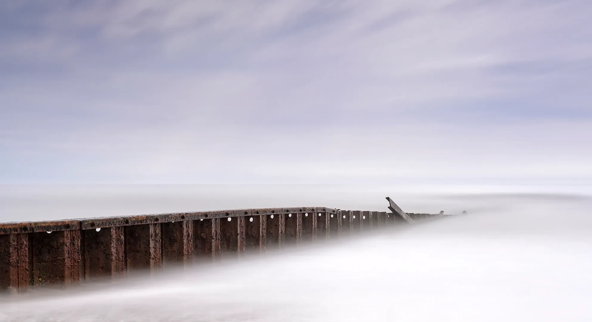 Weathered pier wall disappearing into misty long-exposure surf